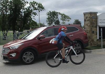 Cyclist riding past a red car on a neighborhood street during daytime.
