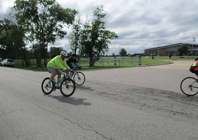 Cyclists riding on a road during Bluebonnet Express event in Texas, with a school in the background.