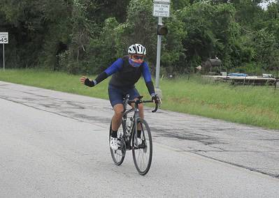 Velo cyclist riding on a rural road, wearing helmet and sunglasses, participating in Bluebonnet Express event.