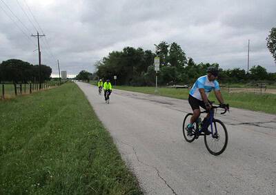 Bicycle riders enjoying a scenic ride on a rural Texas road surrounded by greenery under cloudy skies.
