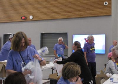 Brightly lit indoor event with volunteers in matching "Bluebonnet Express" shirts exchanging items, highlighting community support and engagement.
