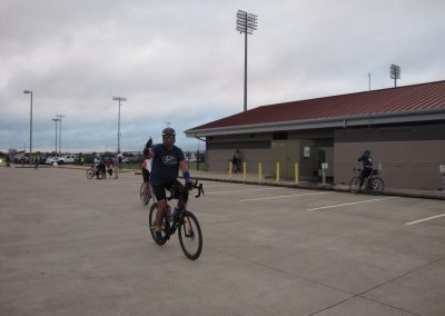 Cyclist in Bluebonnet Express cycling gear waving at camera in parking lot, outdoor sports activity, Texas biking event.