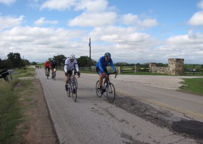 Cyclists riding on a rural road with scenic countryside and blue sky during Bluebonnet Express event.