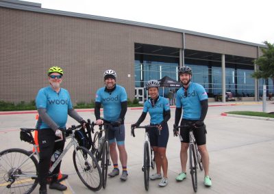 Vibrant Bluebonnet Express cycling team posing with bikes outside a modern building.