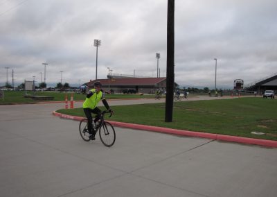 Bicycle rider wearing neon yellow jacket at outdoor sports complex with stadium lighting.