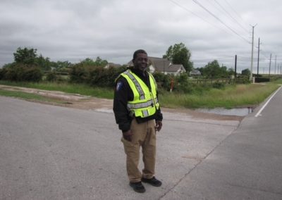 Bright police officer wearing high-visibility vest standing on rural roadside in daylight.