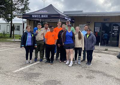 Group of cyclists and scouts gathered outside with a NWCC.BIKE canopy in the background, promoting Bluebonnet Express cycling event.