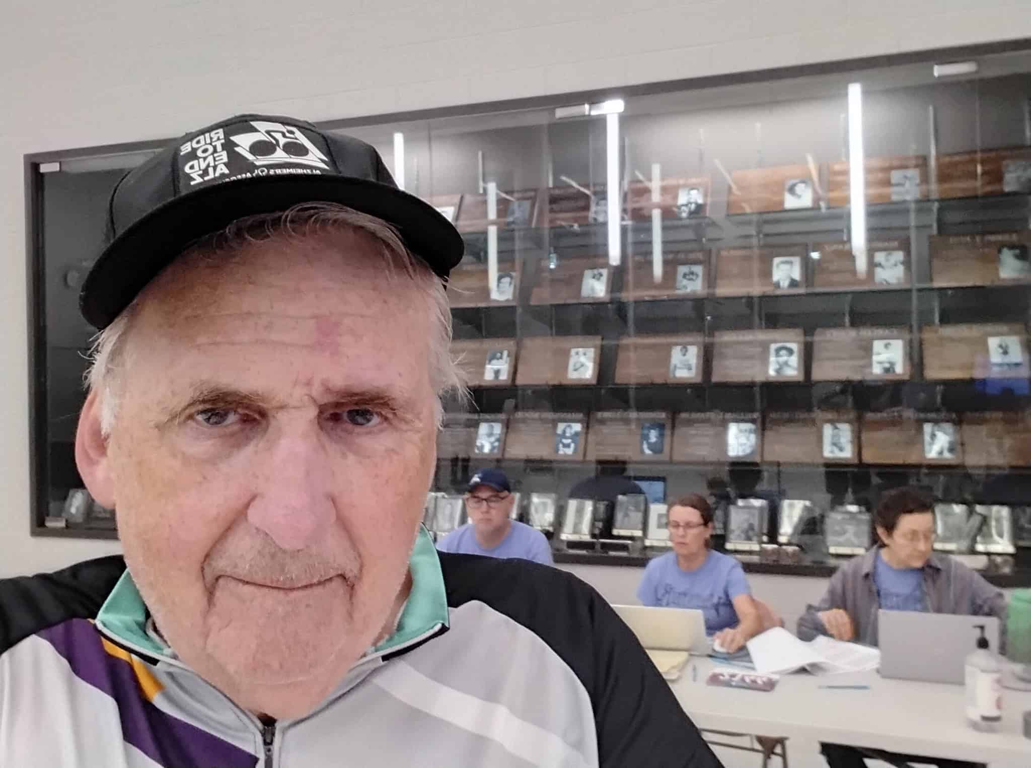 Older man wearing a "Bluebonnet Express" cap taking a selfie at a community event.