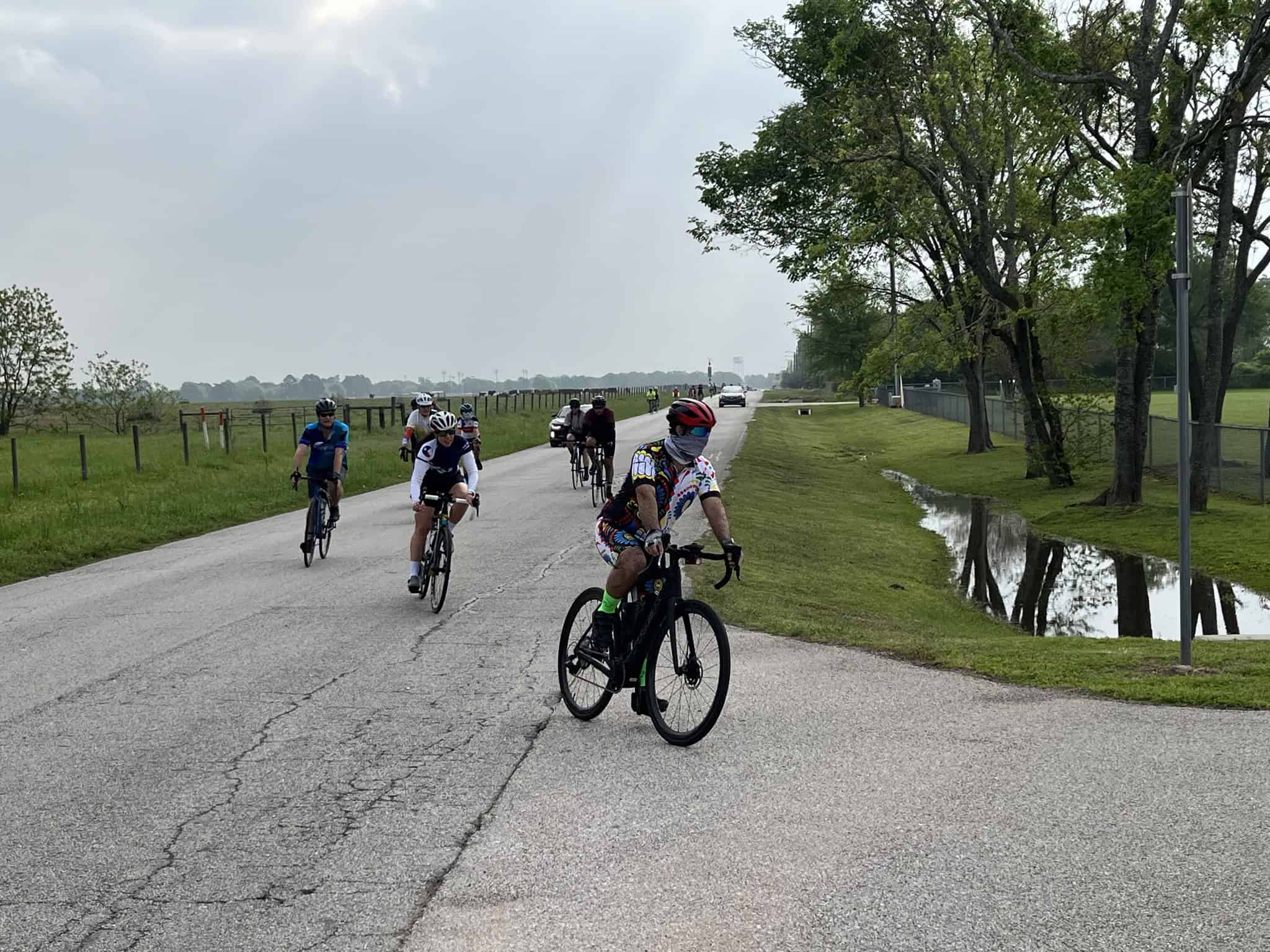 Cyclists enjoying a scenic ride along a country road with trees and a waterway in the background, part of Bluebonnet Express bike tour.