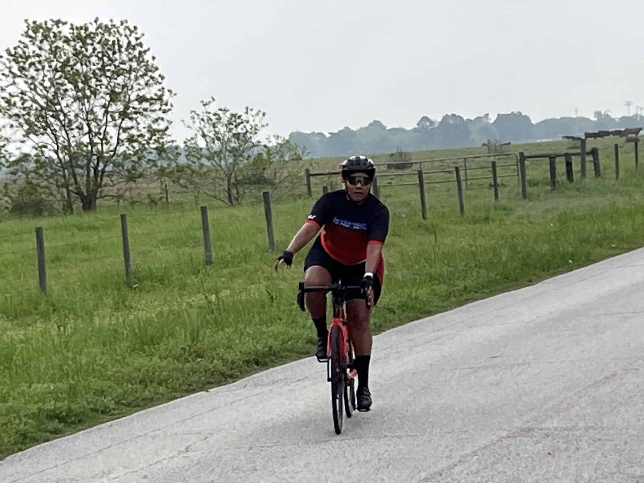 Vibrant bluebonnet-themed cyclist riding on scenic rural bike trail with open fields and green trees.