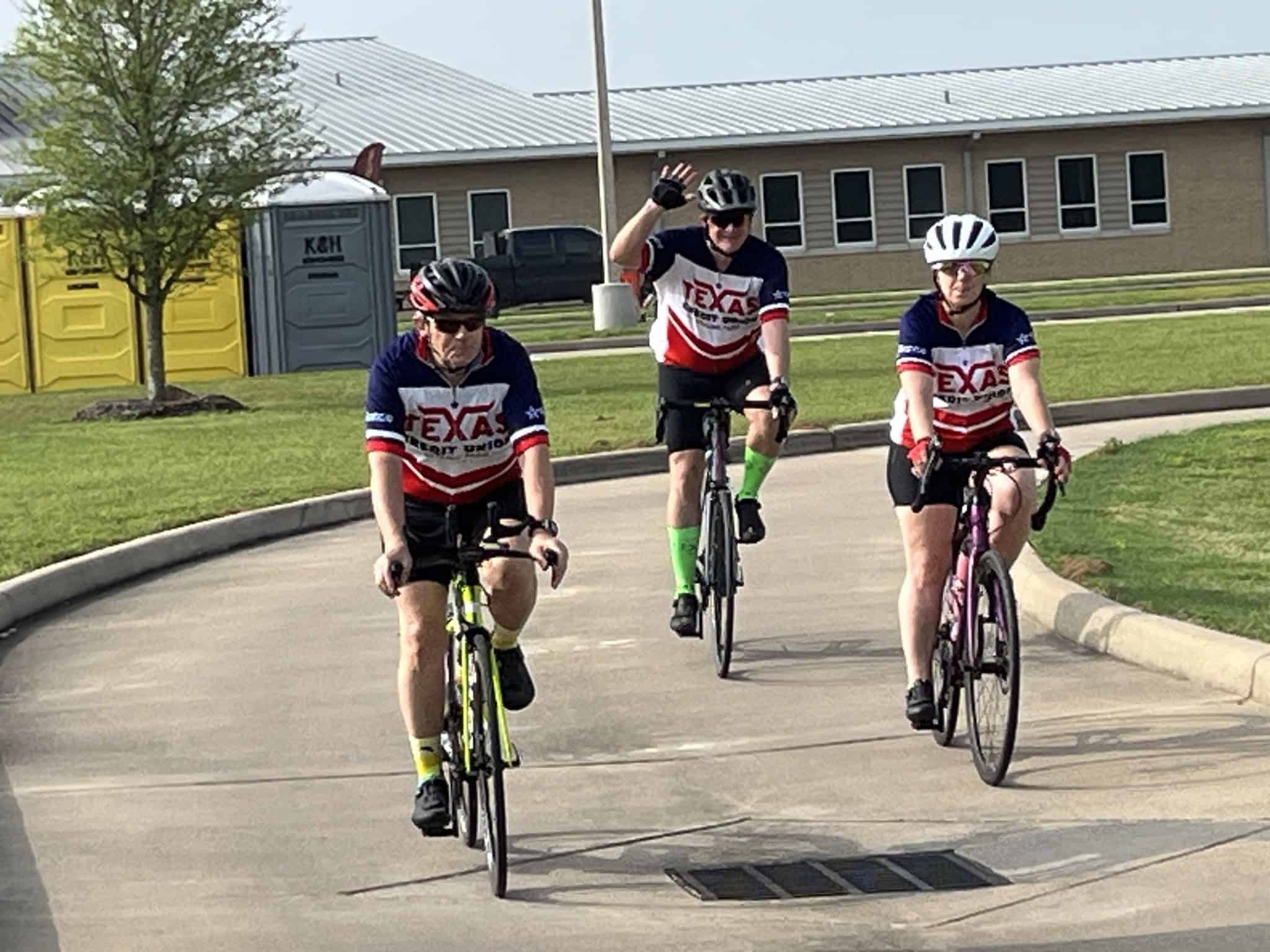 Bicycle riders wearing Texas-themed jerseys cycling together on a paved road.
