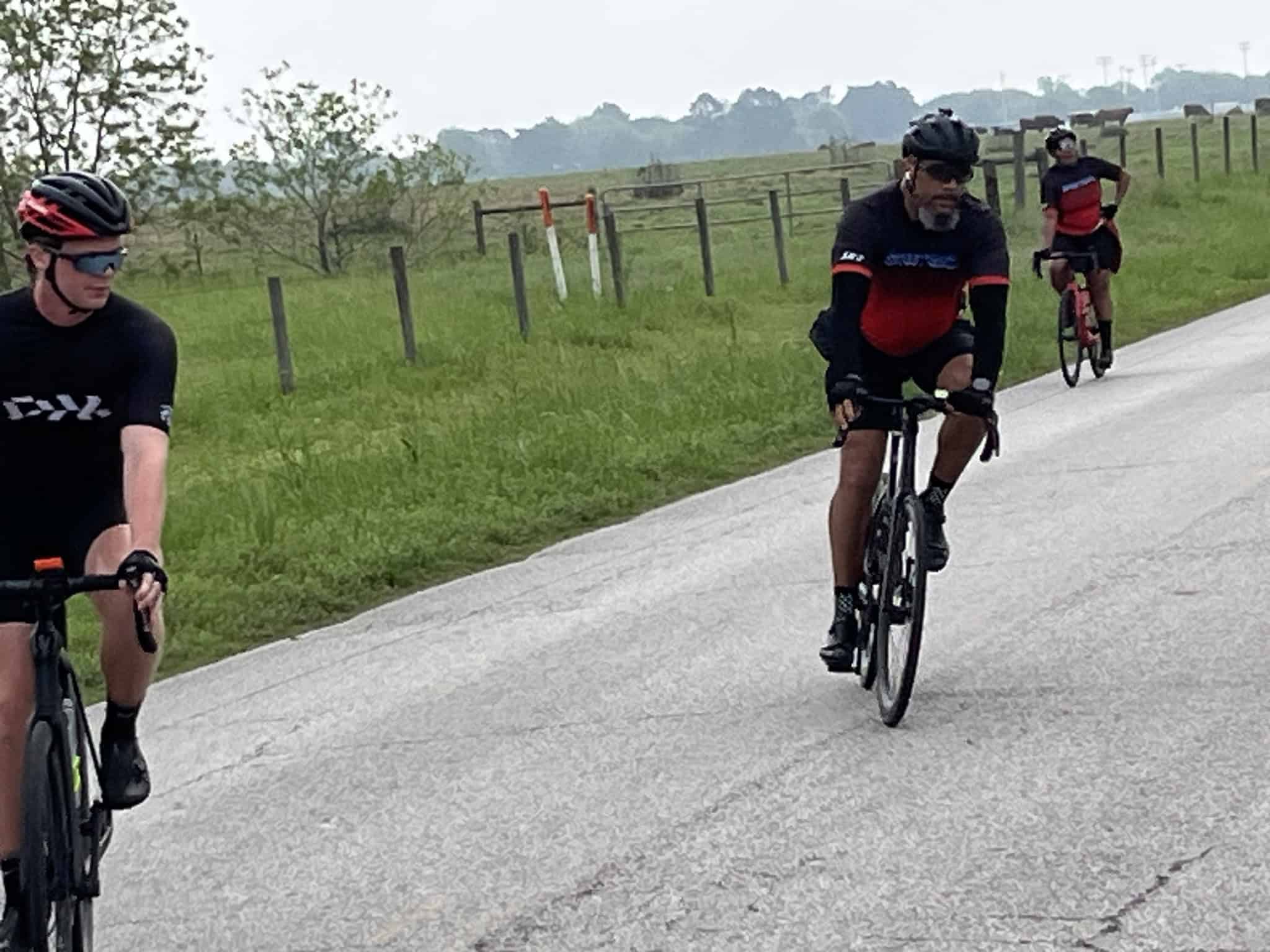 Bright red, blue, and black Bluebonnet Express cycling jerseys on riders on scenic rural road.