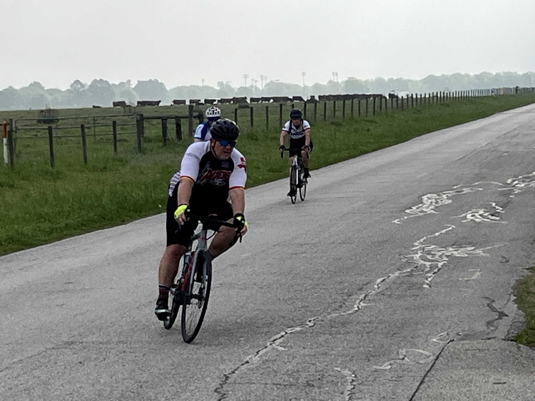 Riders cycling on a rural road with green fields, enjoying outdoor cycling adventure, Bluebonnet Express scenic route.