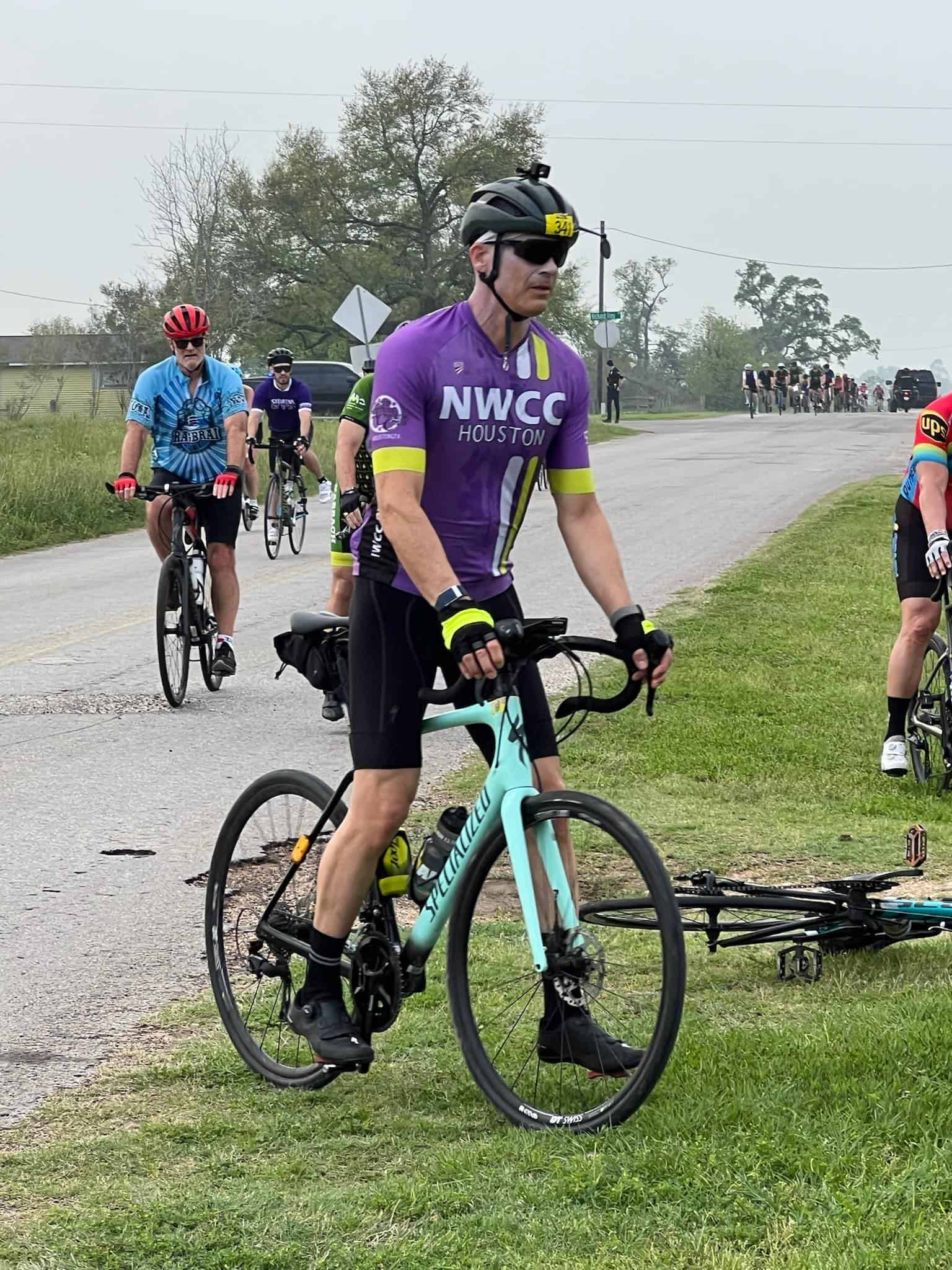 Cyclist wearing NWCC Houston jersey participating in Bluebonnet Express bike ride on scenic rural road.