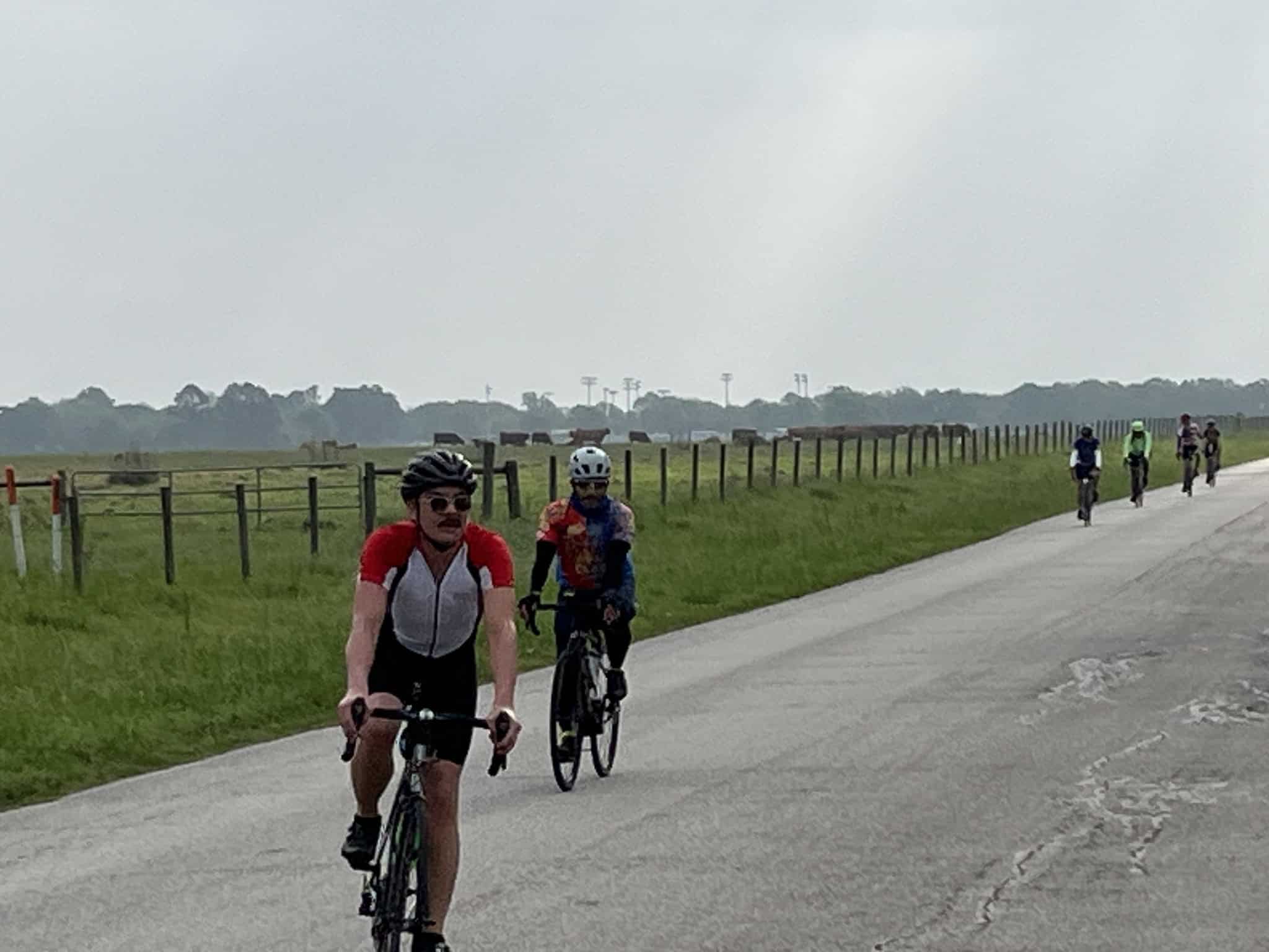 Vibrant cyclists riding along scenic rural Texas road with Greenbelt views, promoting Bluebonnet Express bike tours.