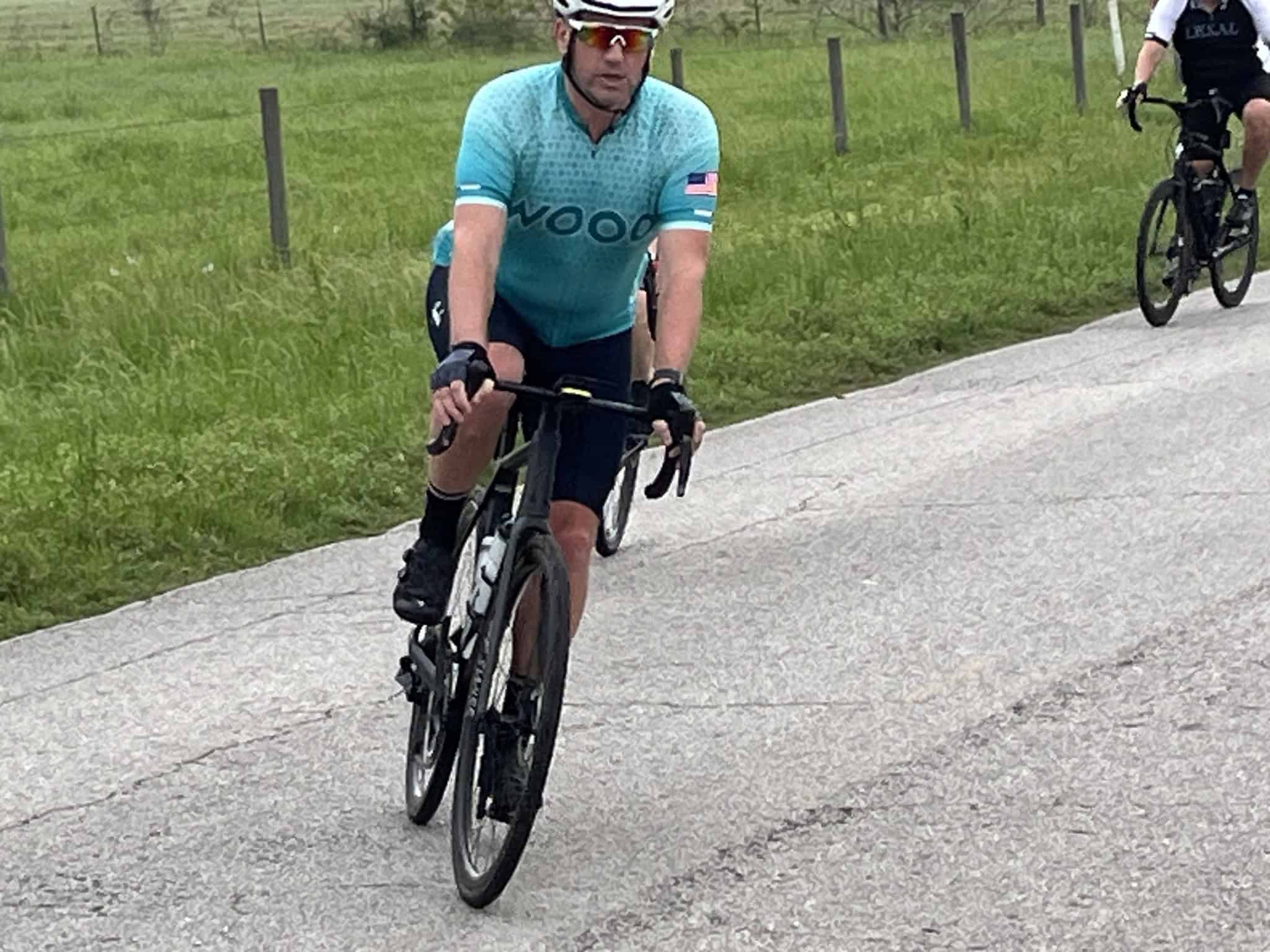 Bright blue cycling jersey with "VOO" logo, male cyclist riding on paved trail in nature.