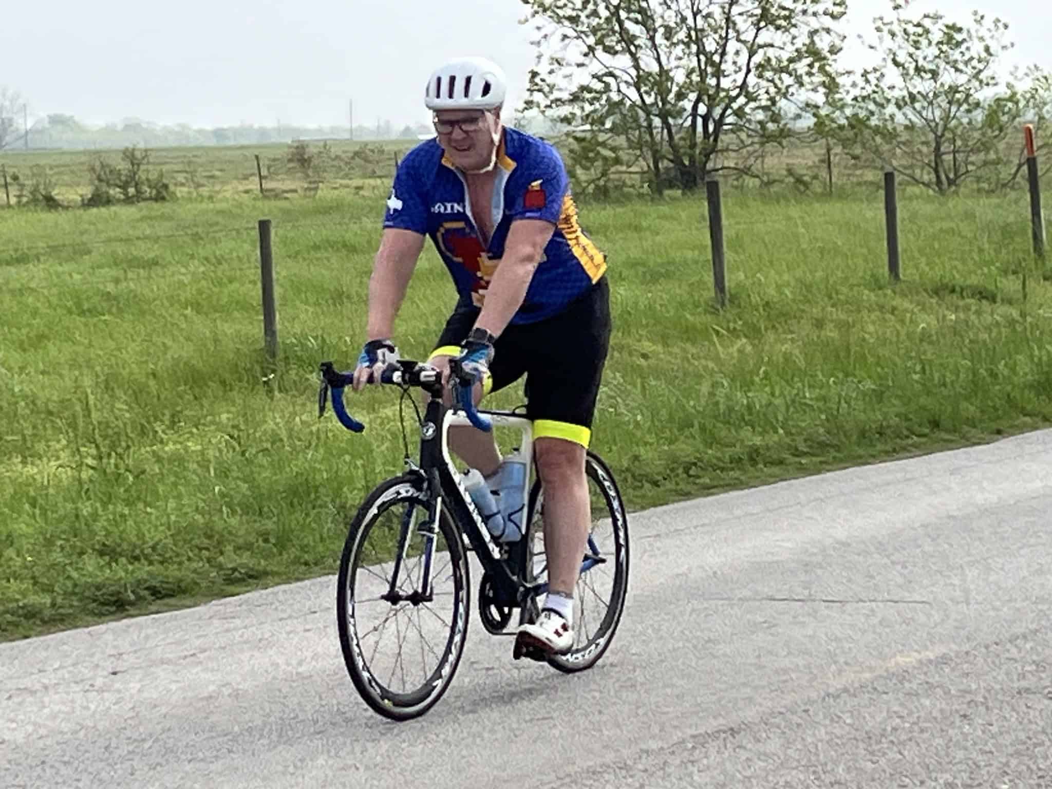 Man riding a Bluebonnet Express branded bike on a rural road during daytime.