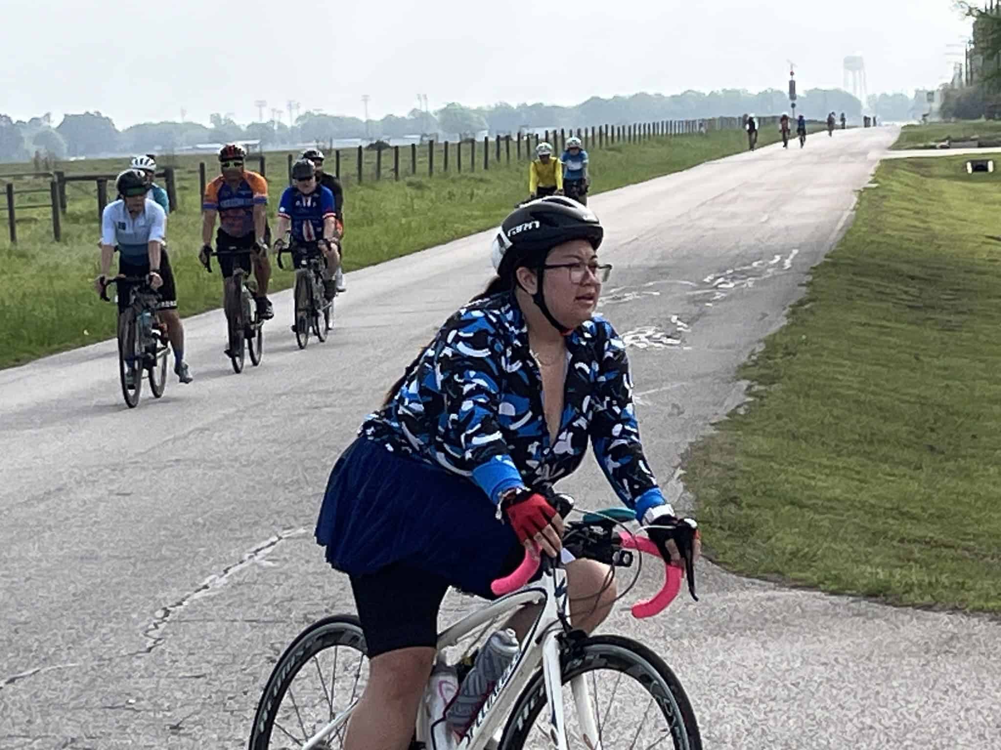 Bright female cyclist with pink gloves riding on a scenic bike trail, part of Bluebonnet Express cycling event.