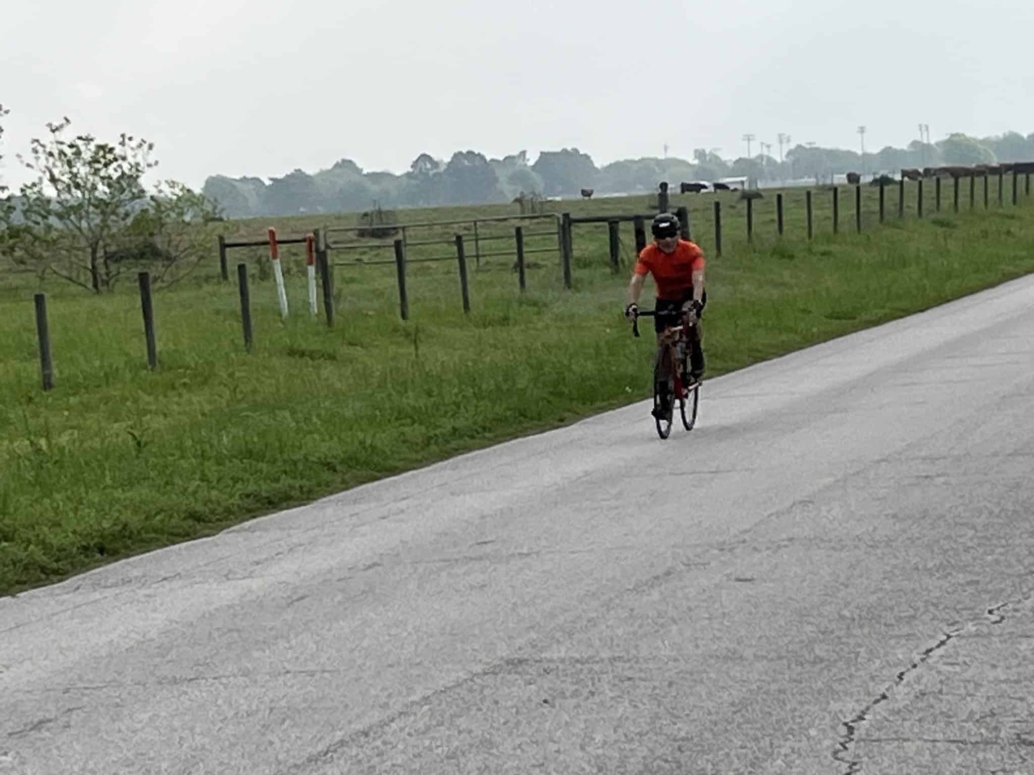 1. Biker riding on scenic countryside paved road with green fields and fences.