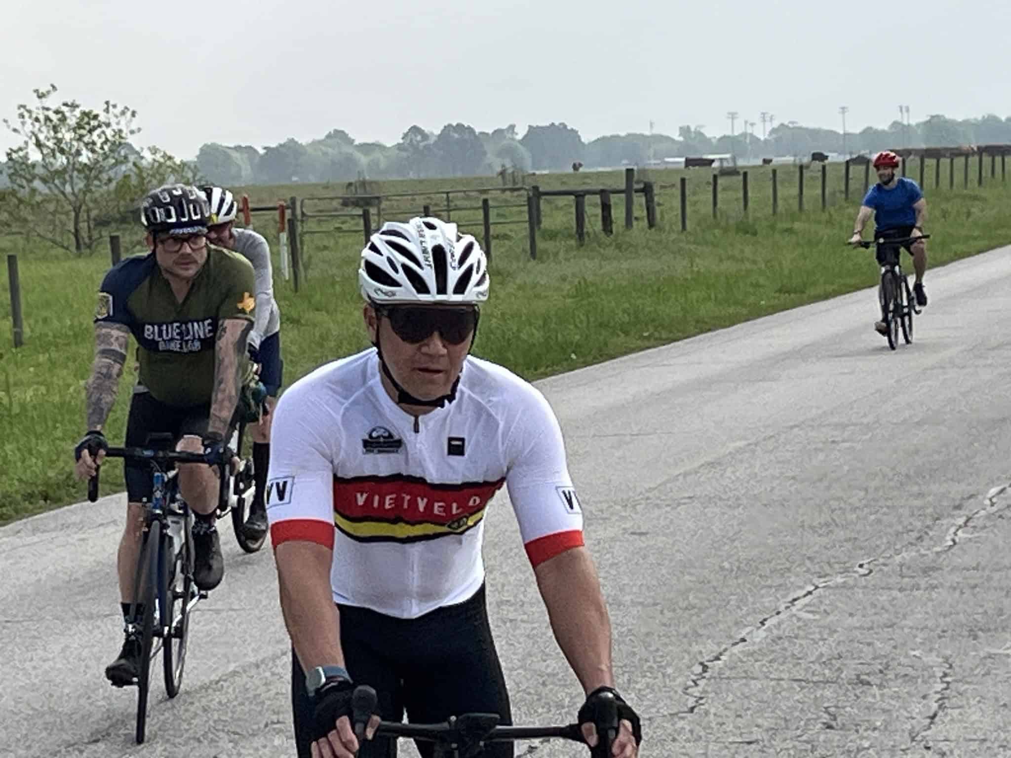 Viet Velo cyclist riding on rural road during group ride with scenic countryside background.