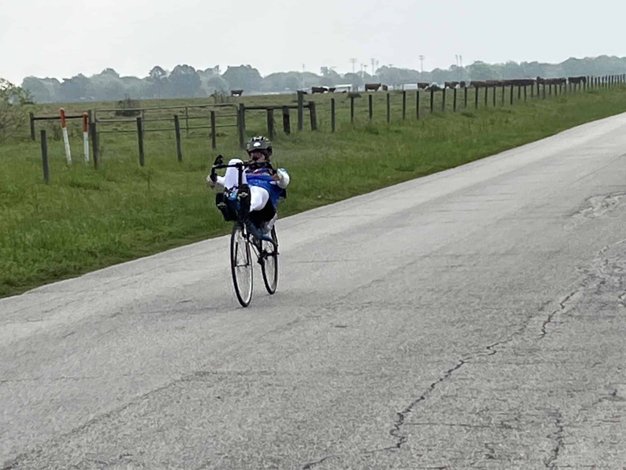 Bicycle rider on rural road with scenic Texas countryside in the background.