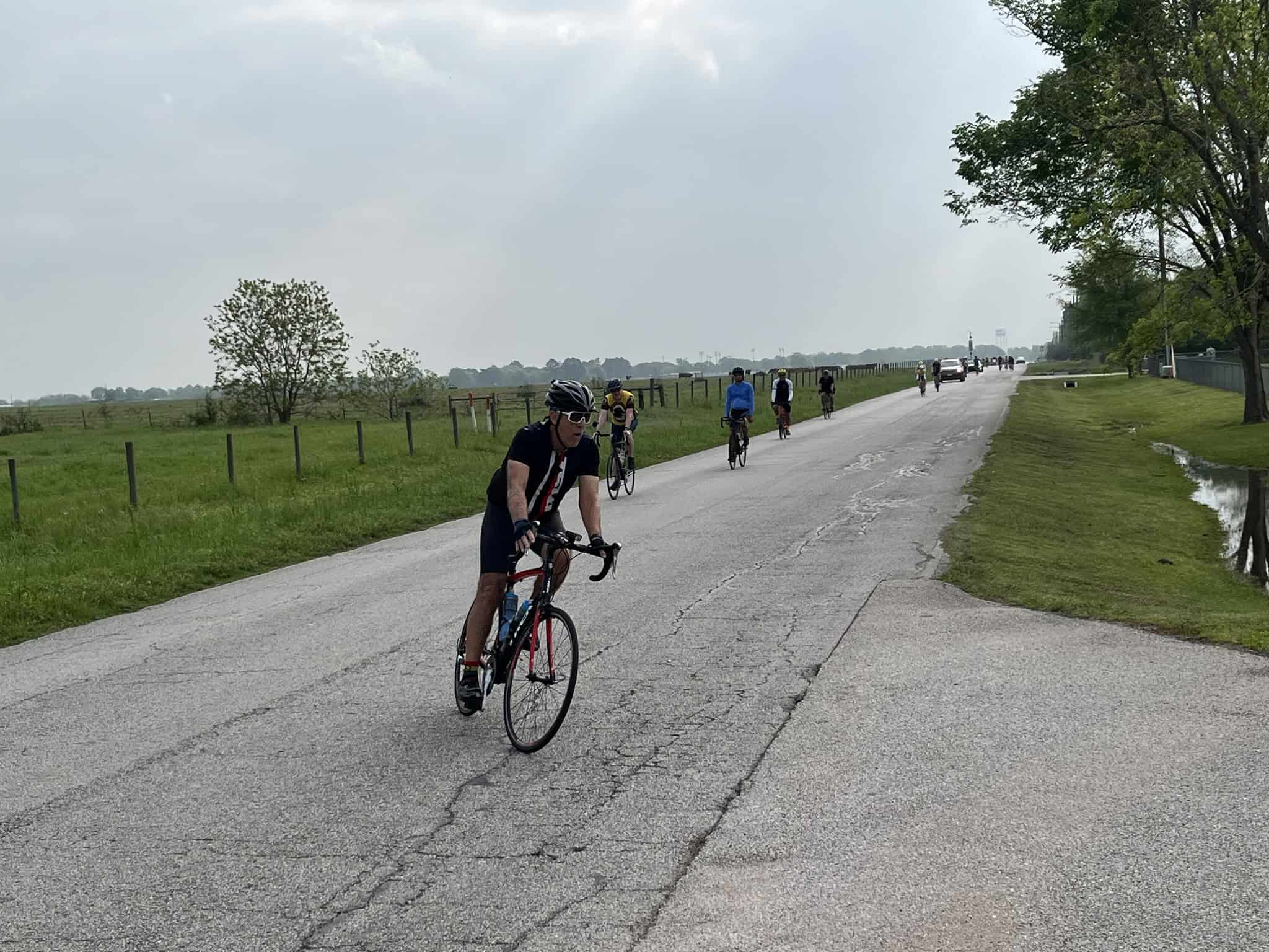 Bike riders on a scenic countryside road with green fields and trees, promoting Bluebonnet Express bike services.