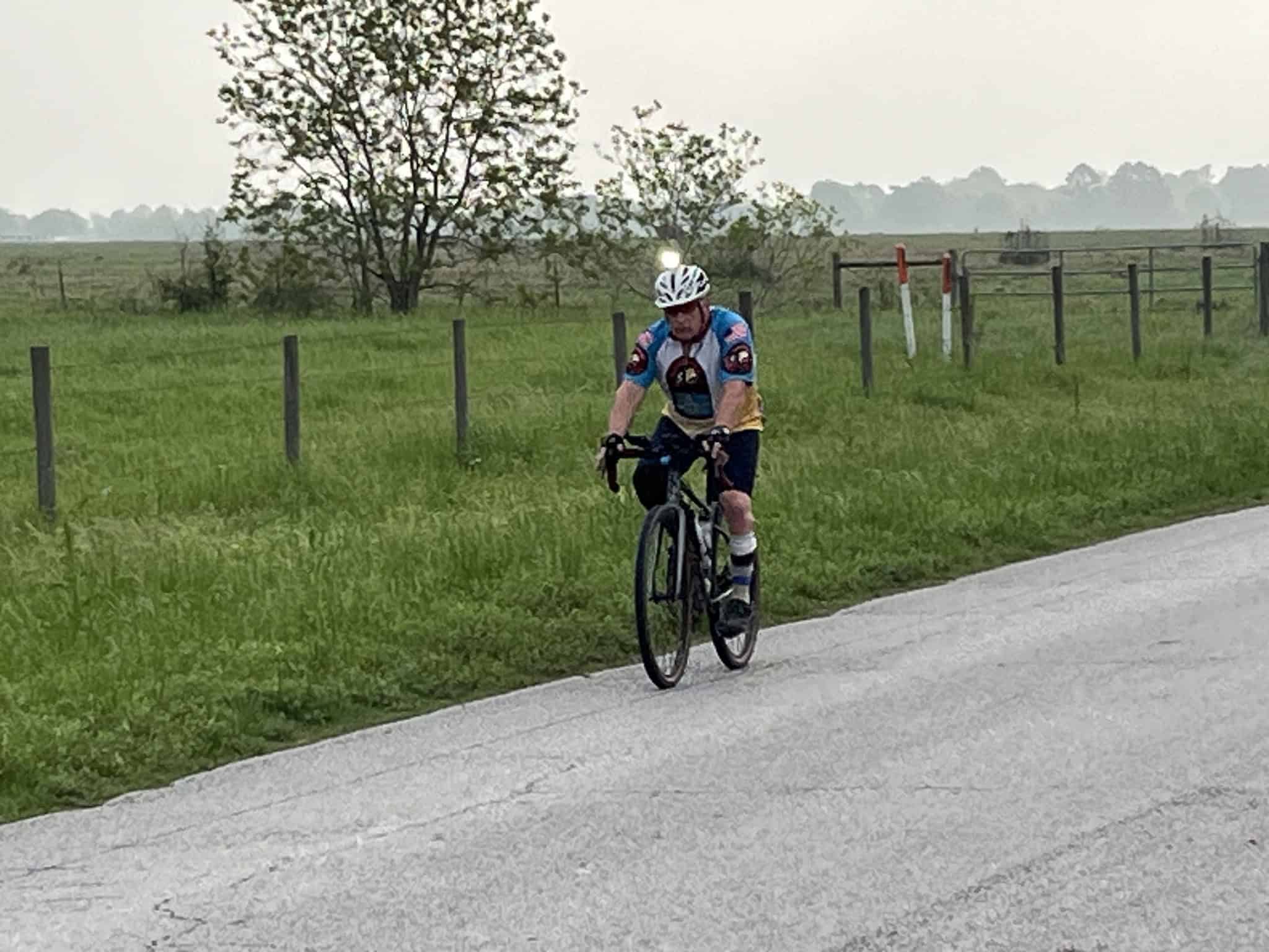 Vibrant cyclist enjoying a scenic rural ride on a paved road with green fields and fencing.