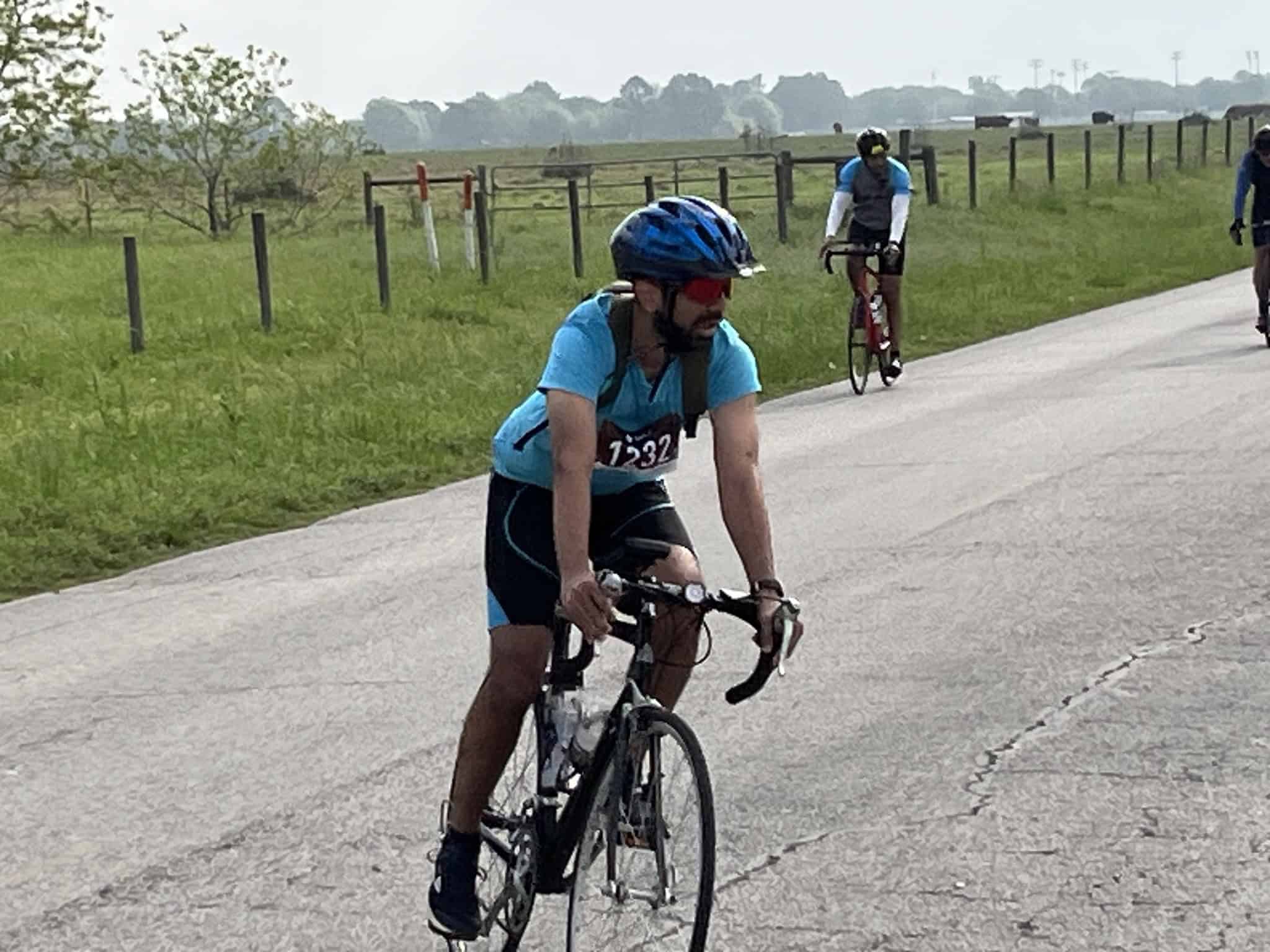 Bike rider in blue team jersey participating in a cycling event with scenic rural background.