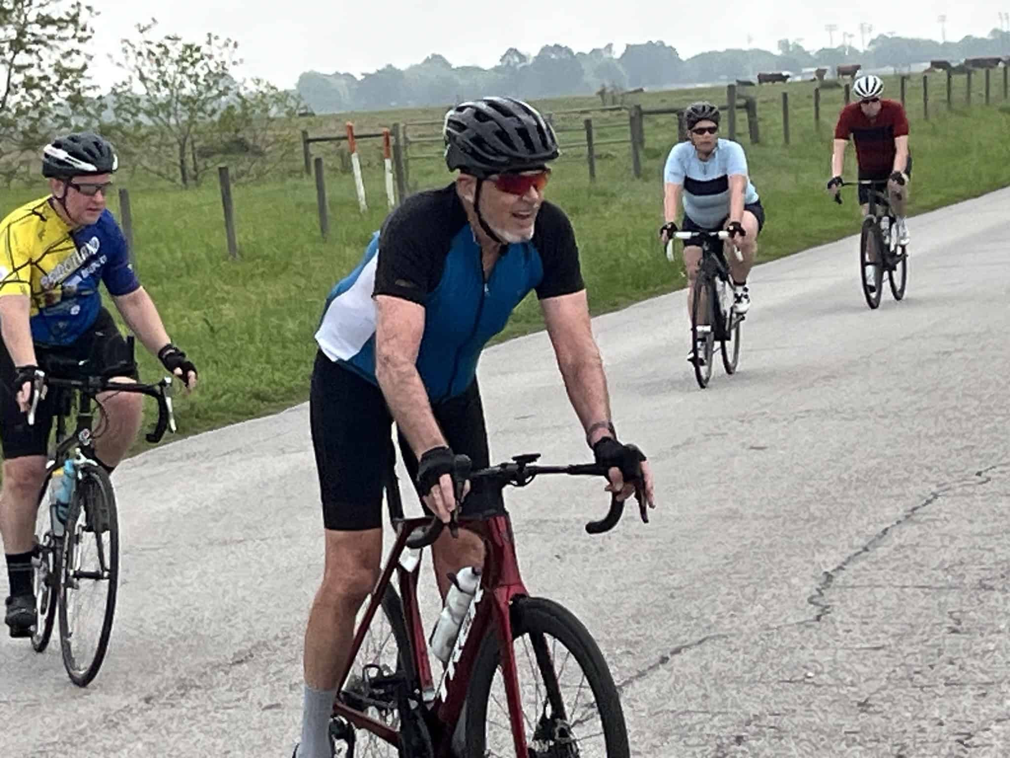 Riders enjoying a scenic bike ride on a rural road with lush green fields and distant cattle.