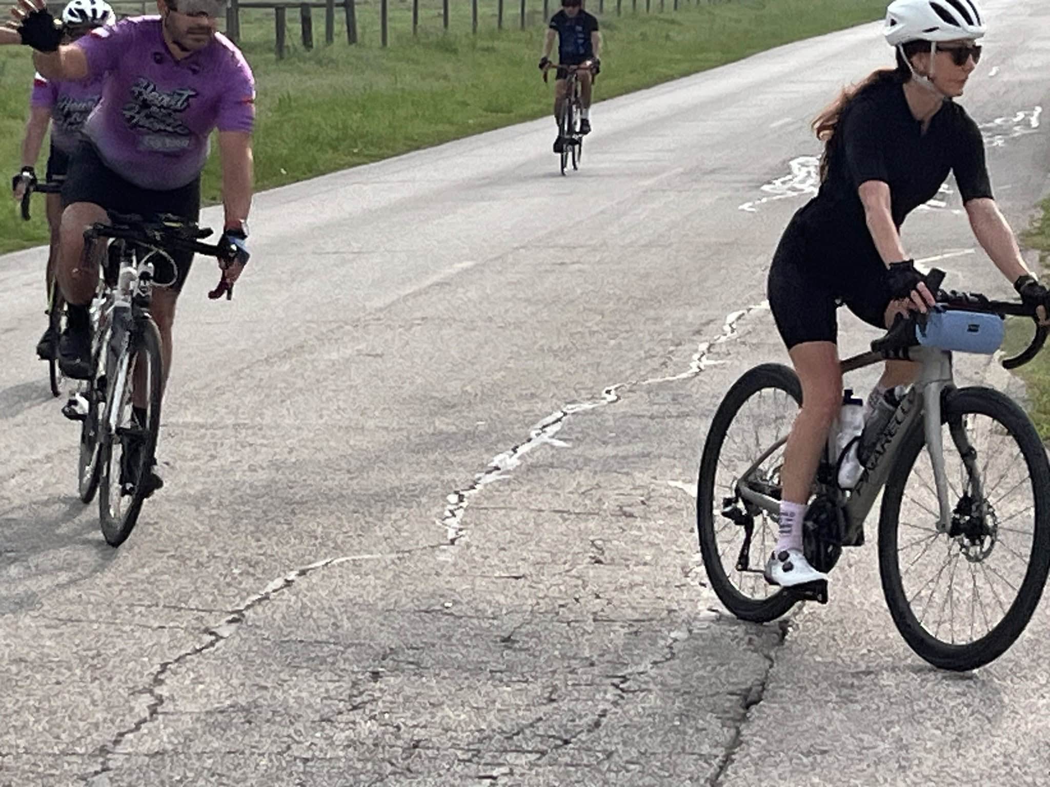 Bright female cyclist riding a modern gravel e-bike on a paved scenic trail with friends during daytime.