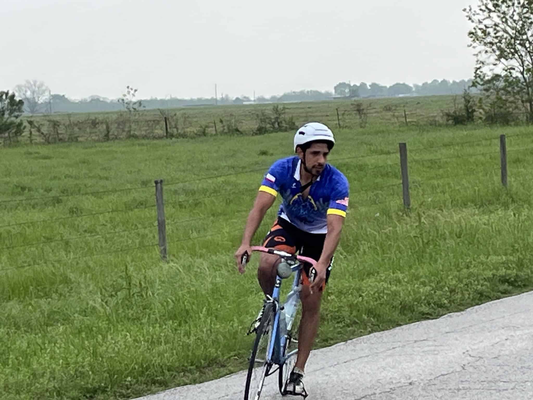 Bright blue cyclist jersey on man riding bike along country road in lush green rural landscape.