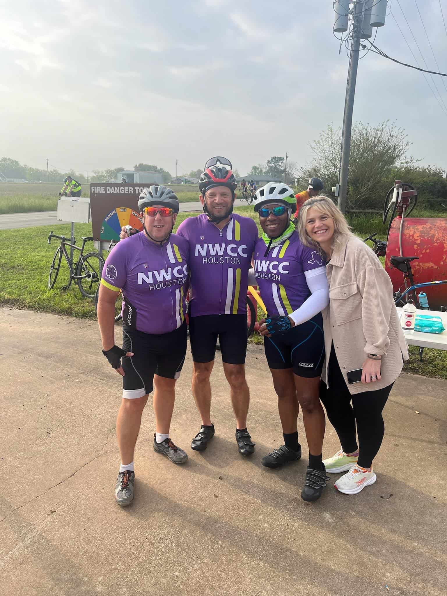 Cyclists in purple NWCC Houston jerseys celebrating at a cycling event, smiling outdoors.