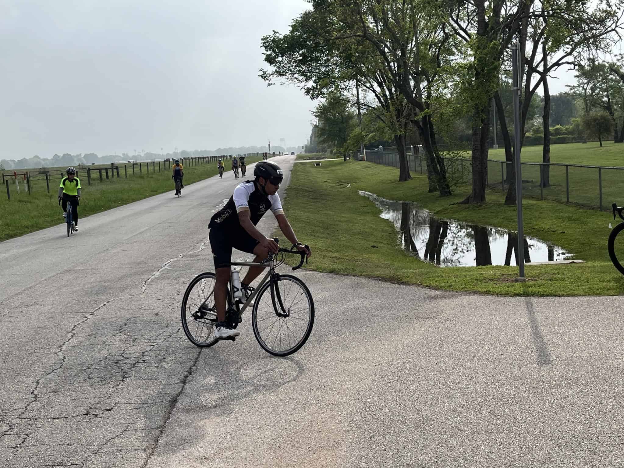Bicycle riders on a scenic outdoor trail near trees and a small water pond, promoting Bluebonnet Express cycling tours.