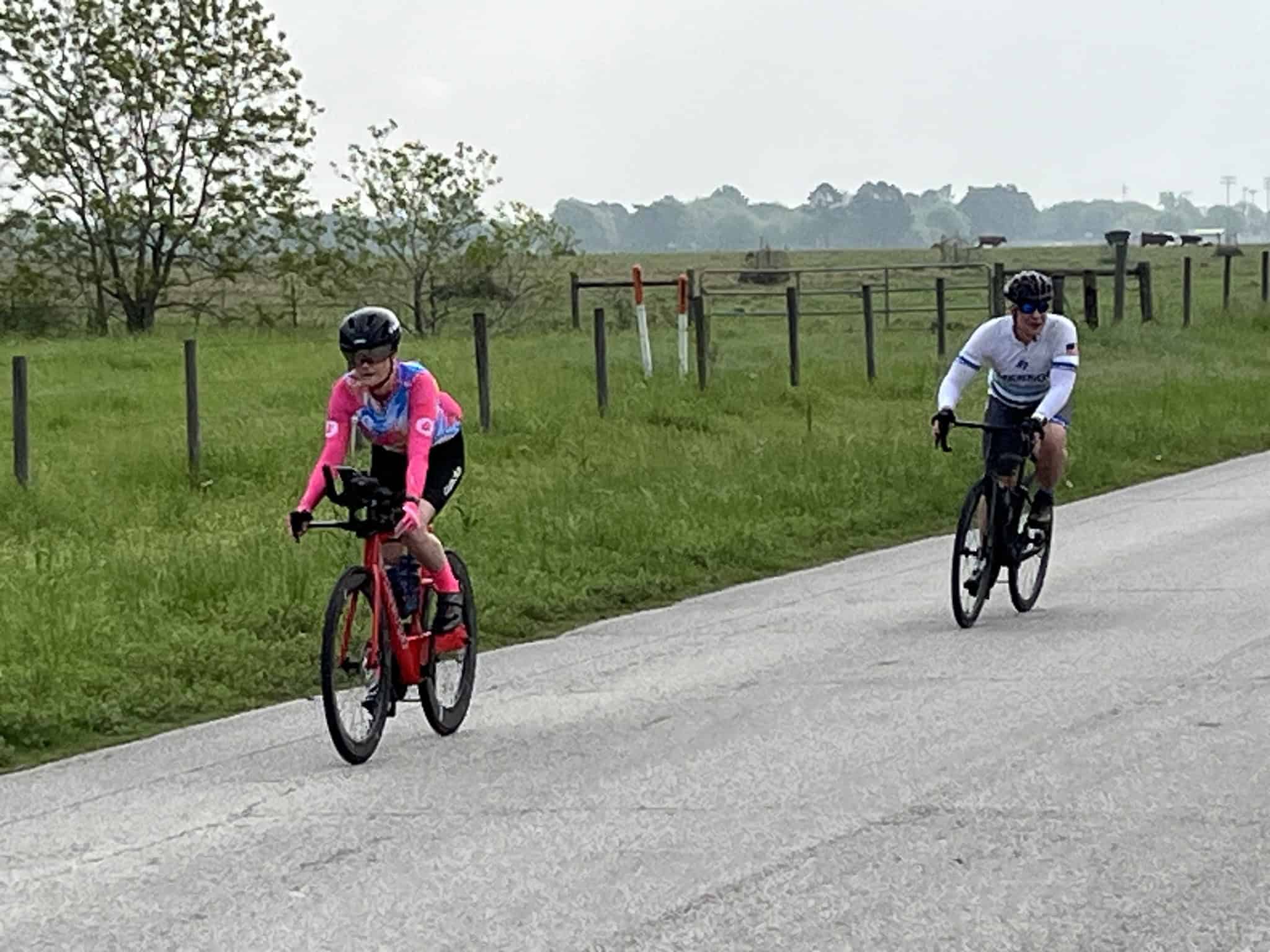 Velo cycling along scenic countryside road with Bluebonnet Express branding in the background.