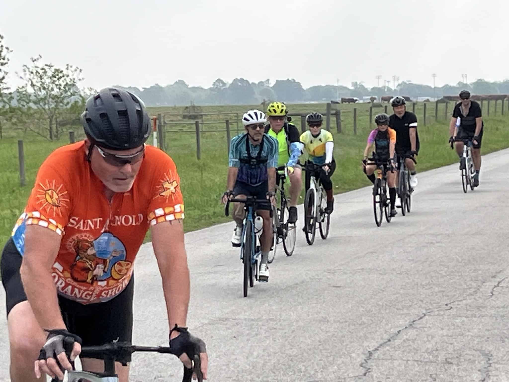 Vibrant group cycling along scenic rural road with lush green fields, enjoying outdoor biking adventure.