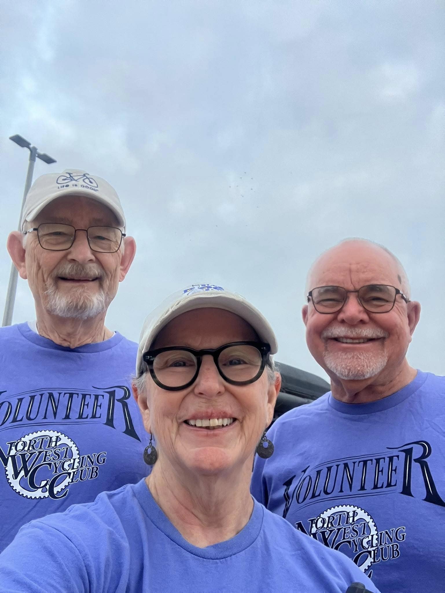 Smiling volunteers in Bluebonnet Express event shirts at a cycling event, outdoors with cloudy sky.