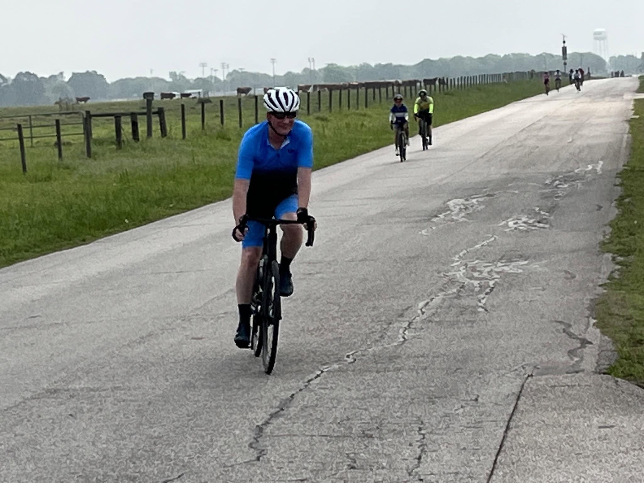 Bike rider in blue cycling jersey on a scenic outdoor bike path with other cyclists in the background.