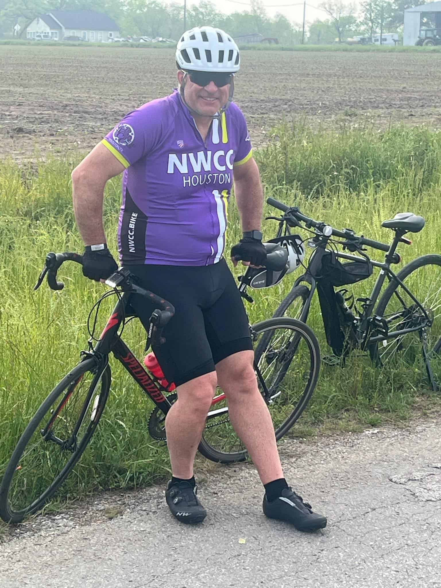 Man in purple NWCC Houston cycling jersey with mountain bike in a rural setting.