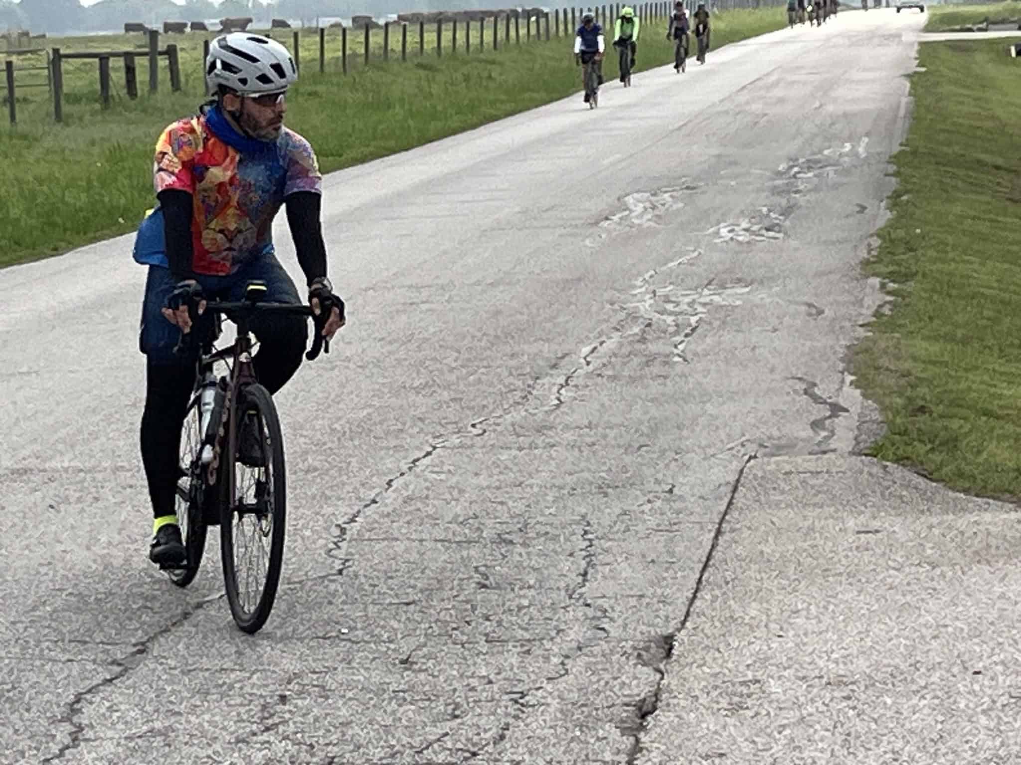 Vibrant cyclist in colorful jersey riding on cracked asphalt trail, scenic outdoor biking route.
