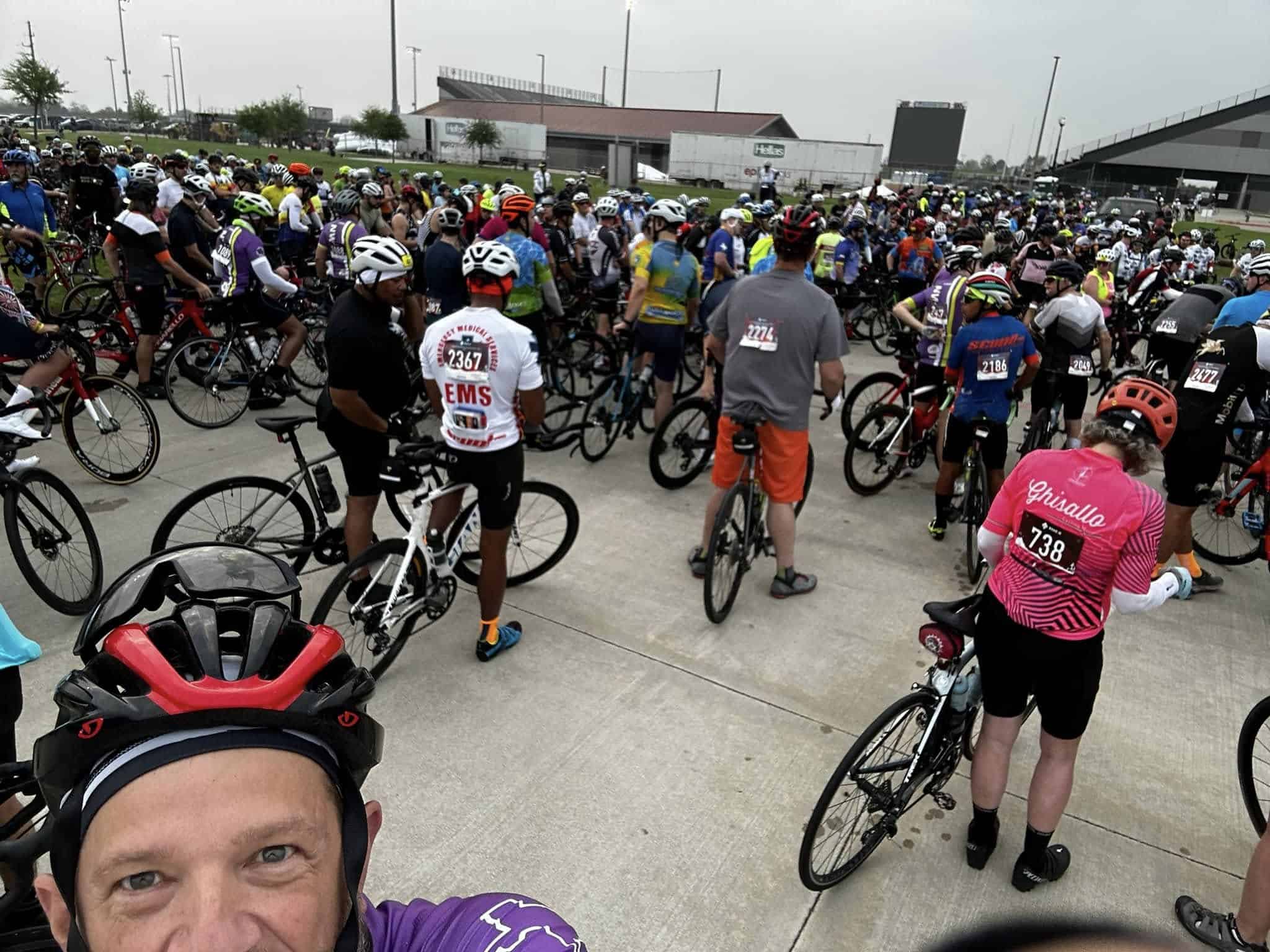Crowd of cyclists at Bluebonnet Express bike event, ready for ride, wearing helmets, jerseys, and race numbers.