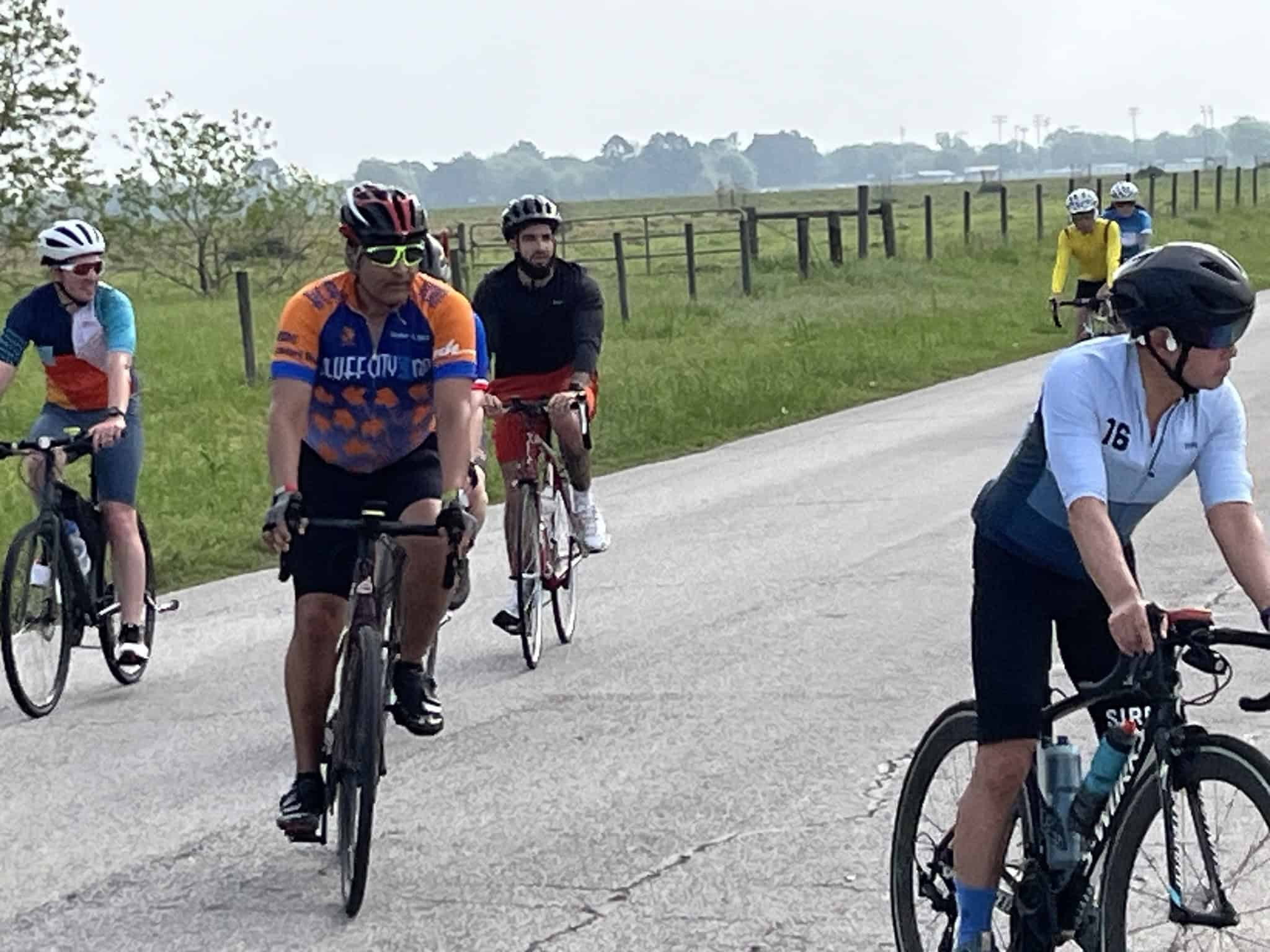 Outdoor group cycling event on scenic rural road with cyclists wearing colorful jerseys and helmets.