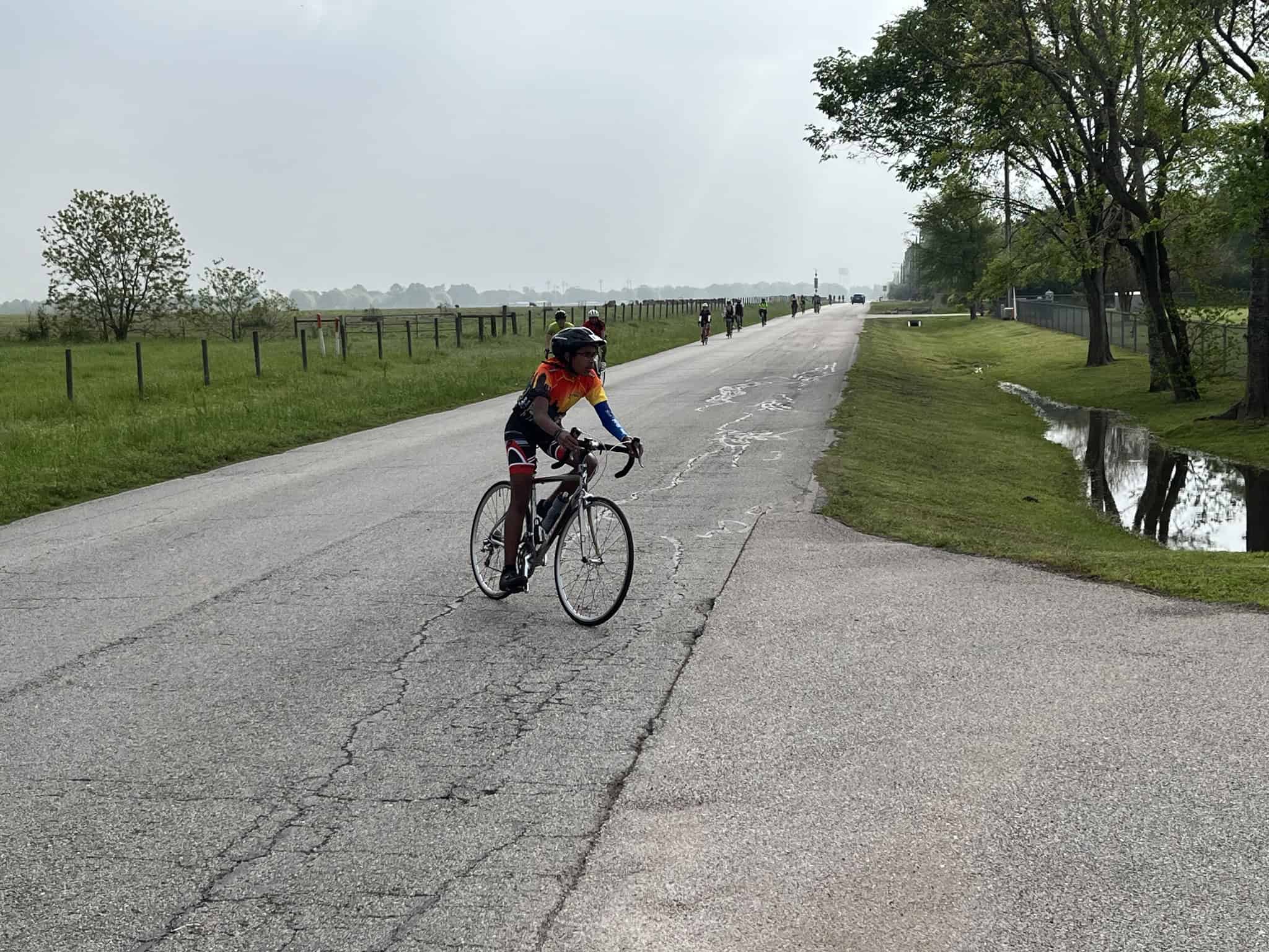 Cyclist riding on a scenic rural road near Bluebonnet Express, with green fields and trees on a cloudy day.