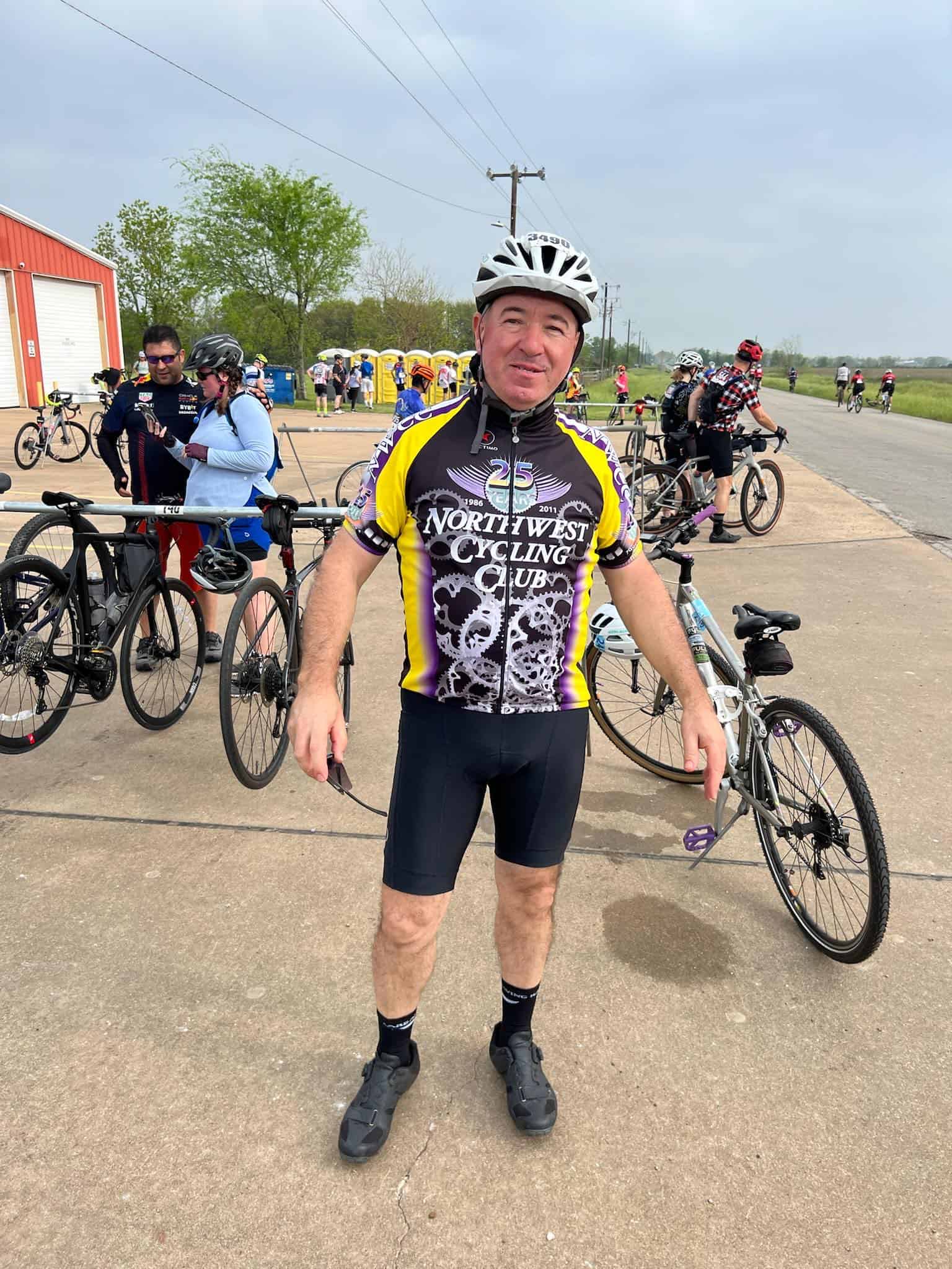 Cyclist at Bluebonnet Express event in Northwest Cycling Club jersey, with bicycles and participants in background.