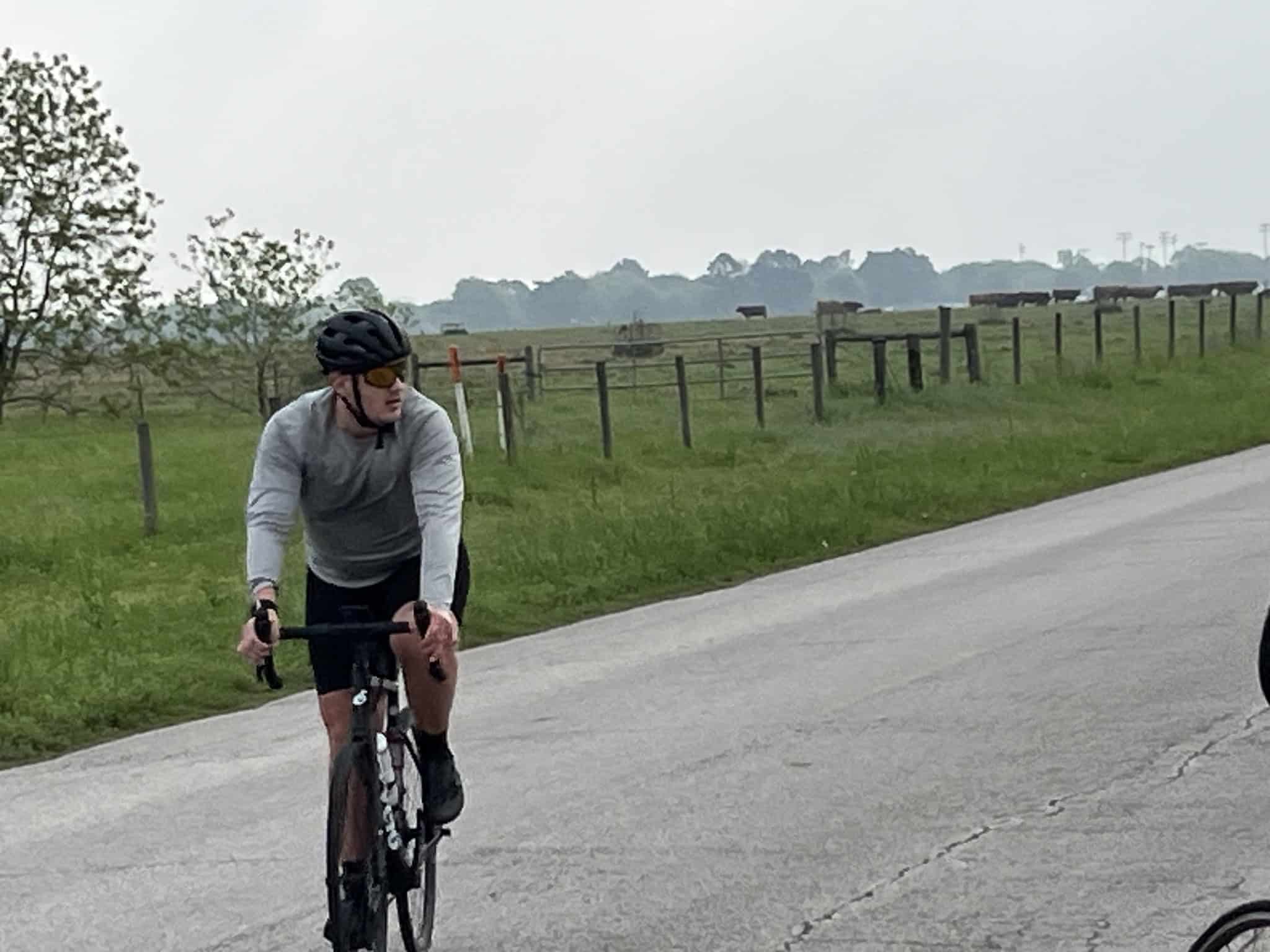High-performance cyclist riding on rural road with scenic farmland background, promoting Bluebonnet Express cycling event.