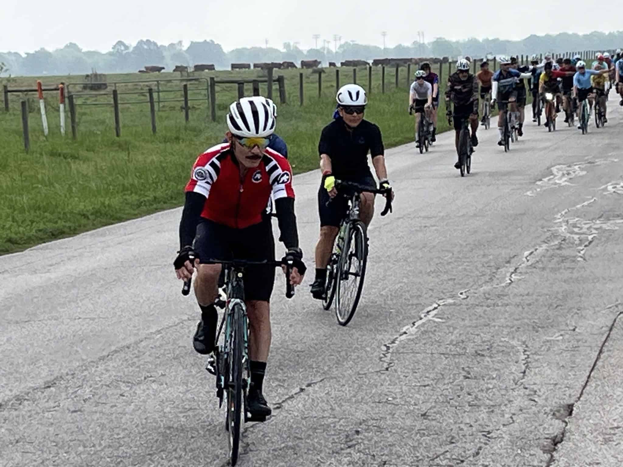 Vibrant group of cyclists riding on rural highway with scenic countryside background, promoting Bluebonnet Express bike event.