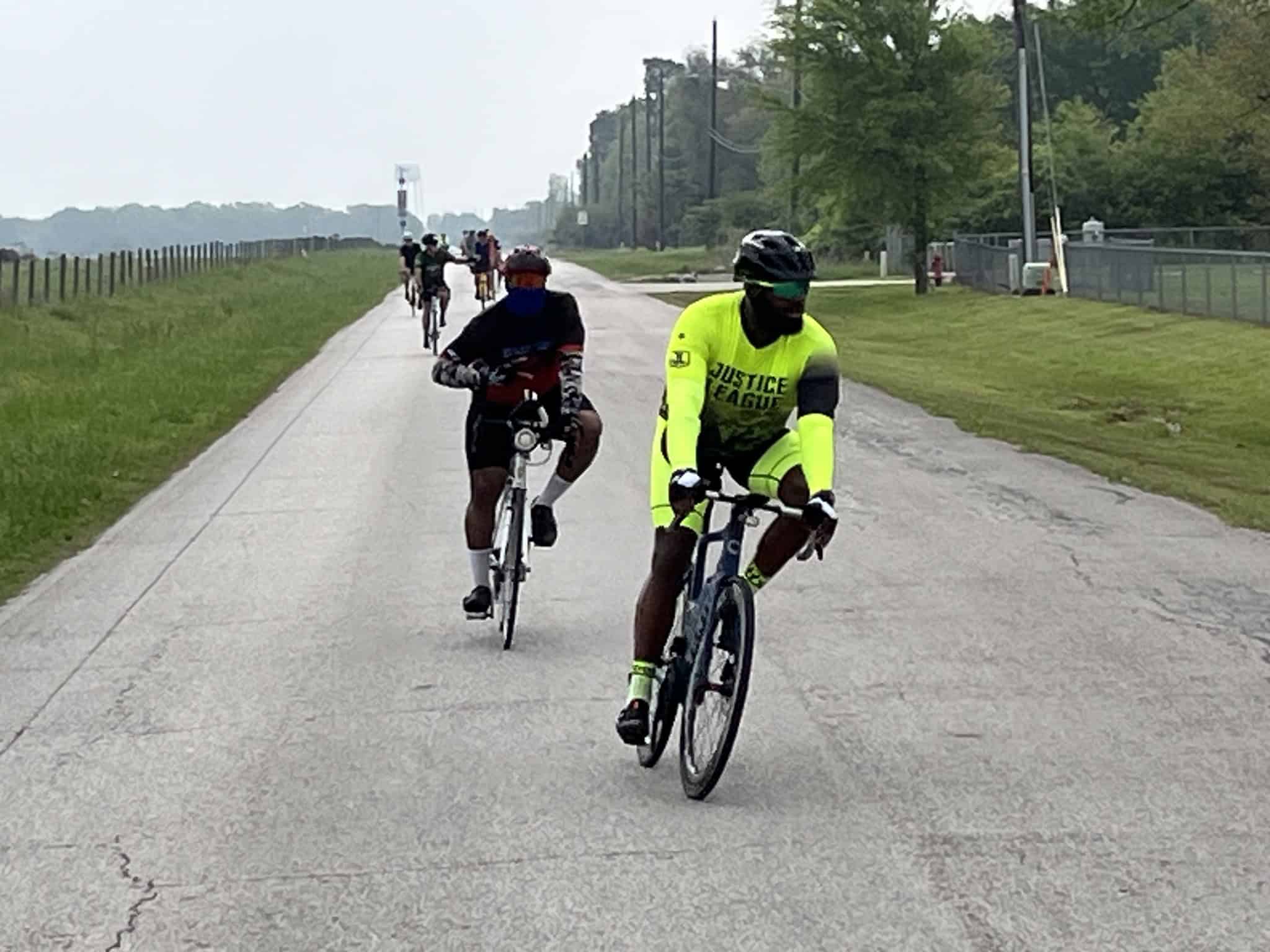 Bright yellow Justice League cycling jersey, group bike ride on scenic trail.
