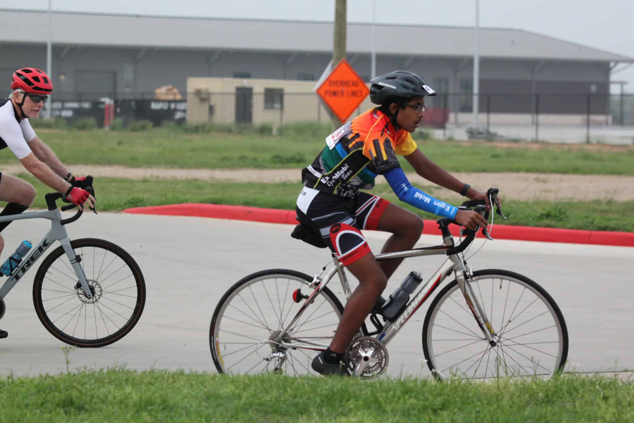 High school cyclists competing in a bike race on a paved track during the day.