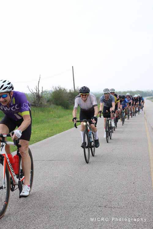 Group of cyclists riding on rural road during Bluebonnet Express cycling event.