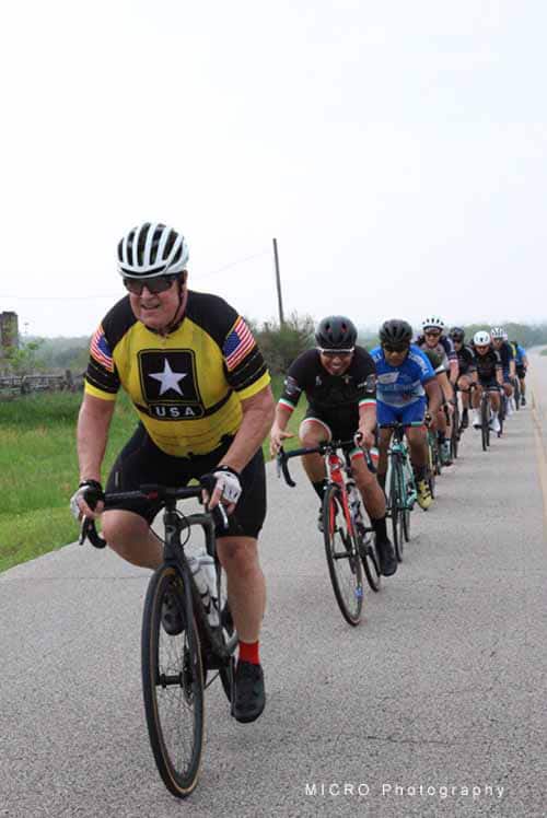 Energetic cyclists riding together on a scenic rural road during Bluebonnet Express event.