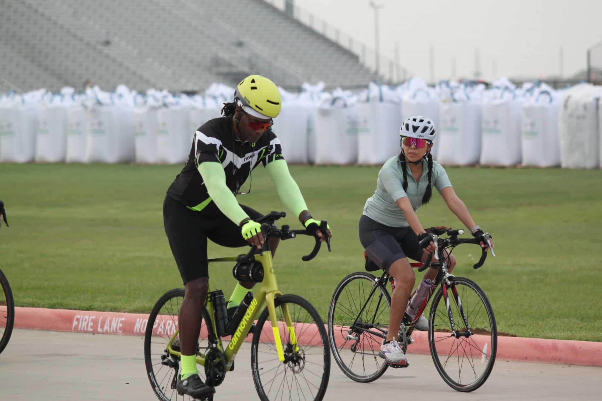 Colorful cyclists riding bikes at Bluebonnet Express event on a grassy field, highlighting cycling and outdoor fitness.